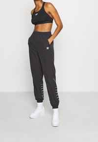 Sujeción deportiva negra y pantalones jogger negros con acentos en franjas blancas. Hechos de una tela ligera, cuentan con una cinturilla elástica y bolsillos.