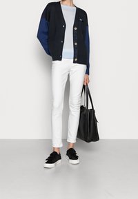 Cárdigan navy con acentos en azul claro, que cuenta con botones y bolsillos. Llevado sobre una blusa azul claro, combinado con pantalones blancos y zapatillas negras.