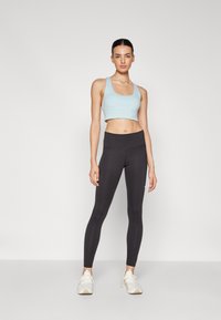Un soutien-gorge de sport court bleu clair et un legging noir taille haute, tous deux en tissu extensible, associés à des chaussures de sport blanches.