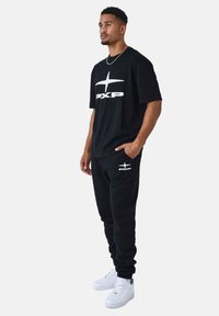 Camiseta de algodón negra y joggers a juego con logo blanco. Las zapatillas son blancas. El conjunto presenta un ajuste relajado y un diseño simple.