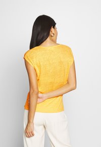 Krátký rukáv, žluté lněné tričko s uvolněným střihem a hladkou texturou, má zaoblený výstřih a jemný slubový vzor.