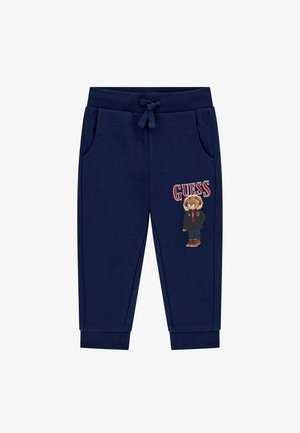 Navy blue sweatpants with an elastic waistband, side pockets, and ribbed cuffs. Features a bear graphic and "GUESS" text on the left leg.