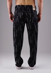 Black denim jeans with a textured pattern of vertical white streaks, five-pocket design, and a logo patch on the waist.