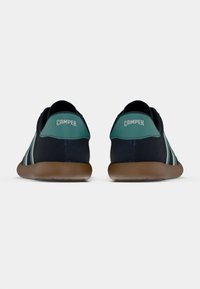 Laivastonsiniset tennarit, joissa on teal-värinen korostus kannassa, valkoiset raidat sivuilla ja ruskea kumipohja; "CAMPER"-logo takana.