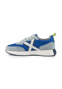 Zapatilla en azul y gris con parte superior de ante y tejido, acentos blancos, suela texturizada y una pestaña verde en el talón.