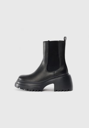 Black leather ankle boots with elastic side panels, thick chunky sole, and textured grip detailing on the outsole. Minimalist design.