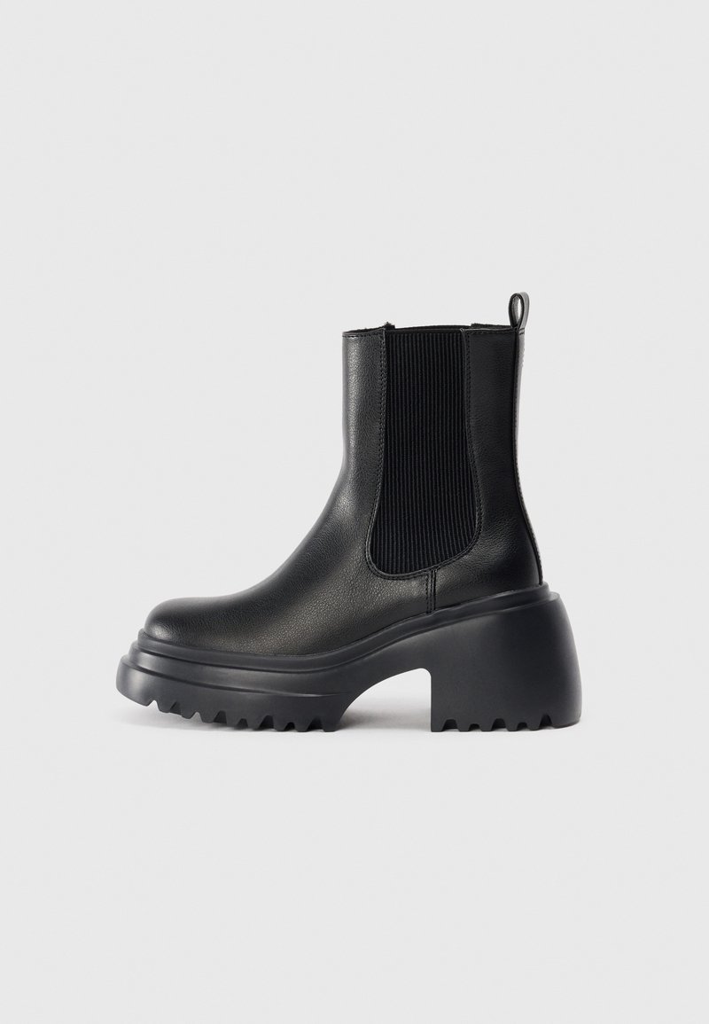 Bottines en cuir noir avec des panneaux élastiques sur les côtés, semelle épaisse et chunky, et détails de texture sur la semelle extérieure. Design minimaliste.