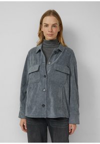 Gray corduroy jacket with two chest pockets, button front, and a relaxed fit. Worn over a gray turtleneck, with a soft texture.