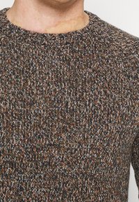 Strickpullover mit Rundhalsausschnitt, strukturierter mehrfarbiger Stoff in Erdtönen, durchzogen von braunen, grünen und cremefarbenen Fäden.