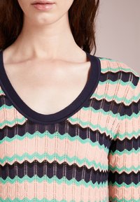 Stickad tröja med en djupt marinblå krage. Funktioner zigzag-ränder i persika, svart och mintgrön. Texturerat mönster med öppen väv.