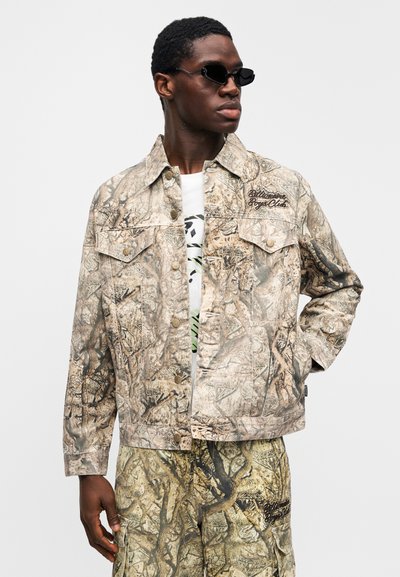 Τζιν μπουφάν με σχέδιο παραλλαγής σε μπεζ και καφέ αποχρώσεις, με δύο τσέπες στο στήθος, μεταλλικά κουμπιά και κεντημένη επωνυμία στον ώμο.