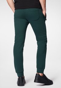 Ciemnozielone dresy z miękkiego materiału, o dopasowanym kroju, z ściągaczami na mankietach i tylną kieszenią. W zestawie z czarnymi sneakersami.