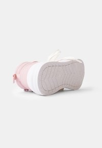 Roze en witte sneaker met een gestructureerde zool, gevoerde delen, elastische banden en een lus aan de achterkant voor gemakkelijk aan- en uittrekken.