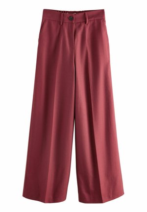 Person wearing high-waisted, elastic-backed, dark red trousers with hands in side pockets and a tucked-in black top.