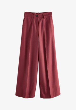 Osoba nosiaca tmavomodré nohavice s vysokým pásom a elastickým zadným dielom, ruky v bočných vreckách a zastrčené čierne tričko.