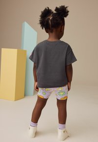 Szary, krótki rękaw t-shirt, kolorowe, kwiatowe szorty rowerowe w pastelowym fioletowym kolorze, białe wysokie buty i liliowe skarpetki.