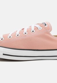 Růžové plátěné tenisky s bílými očka a tkaničkami. Mají gumovou podrážku s černým pruhem a texturovaný vnější povrch.