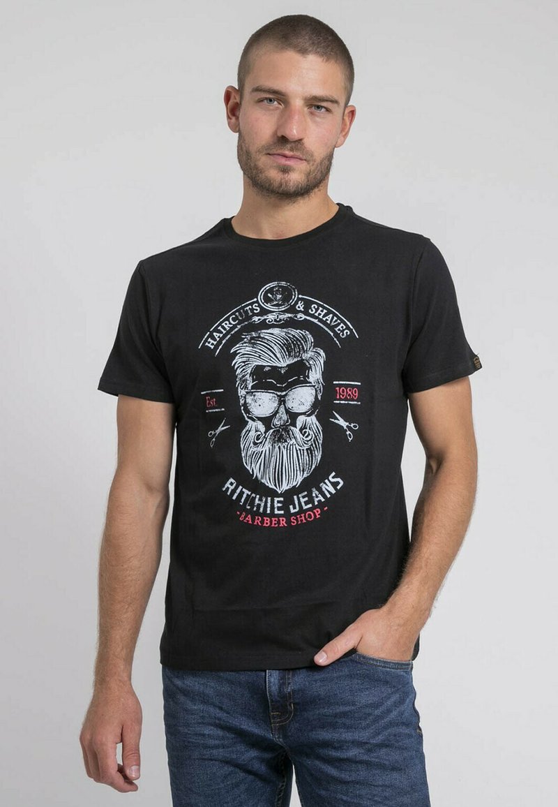 T-shirt en coton noir avec un imprimé graphique d'un crâne avec des lunettes, des ciseaux et du texte, associé à un jean bleu.