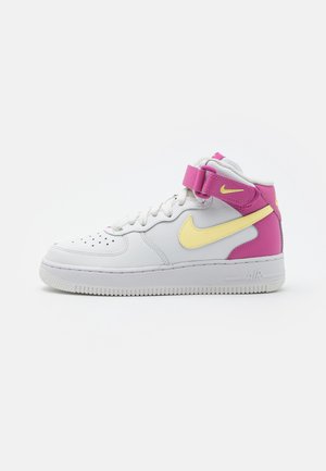 Białe wysokie buty sportowe z żółtym logo Nike w kształcie znaku, różową paskiem przy kostce i różowymi akcentami na pięcie, na neutralnym tle.