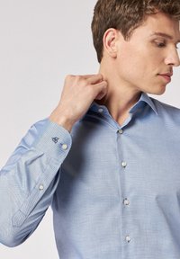 Camicia button-up azzurro chiaro con un piccolo motivo a quadretti testurizzati. Presenta un colletto classico e un logo ricamato sul polsino.