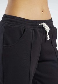 Pantalones de chándal negros hechos de tejido suave, con una cintura elástica ajustable y bolsillos laterales. El diseño incluye un pequeño detalle de logo.