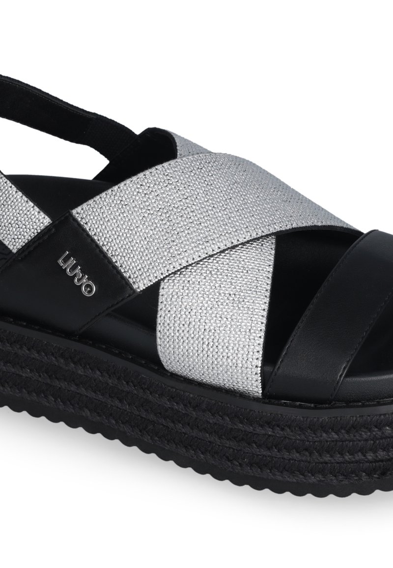 Sandales compensées noires avec des brides tissées en argent texturé et des accents en cuir noir, dotées d'une semelle tissée épaisse pour un bon support.