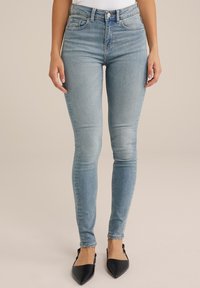 Ljusblåa skinny jeans i denim med hög midja, subtila blekning och fem fickor, kompletterade av svarta spetsiga skor.