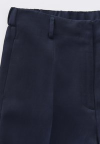 Pantalons en tissu bleu marine avec une texture lisse, présentant un devant plat, des passants de ceinture et une poche latérale sur la droite.