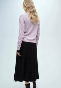 Lila långärmad tröja i avslappnad passform som matchas med en svart plisserad kjol. Kjolen har en strukturerad design.