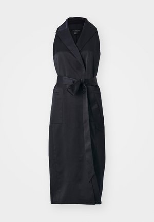 Zwarte mouwloze wikkeljurk van gladde stof met een kraag, een strikceintuur op de taille en twee voorzakken.