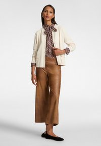 Elfenbeinfarbener Cardigan, gemusterte braune Bluse mit Schleife, braune weit geschnittene Hose und schwarze Ballerinas. Weiche Texturen, taillierte Passform und geschichtetes Design.