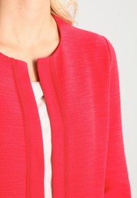 Red textured jacket with a mandarin collar, featuring a sleek design and subtle stitching detail along the front opening.