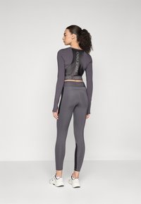 Gray long-sleeve shirt with a black mesh back and "NIKE PRO" logo, paired with gray leggings and white athletic shoes, viewed from behind.