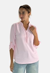 Jasnoróżowa koszula zapinana na guziki z kołnierzykiem mandaryńskim, rękawami o długości trzech ćwiartek z możliwością podwinięcia, detalem kieszeni, teksturowanym materiałem i luźnym krojem.