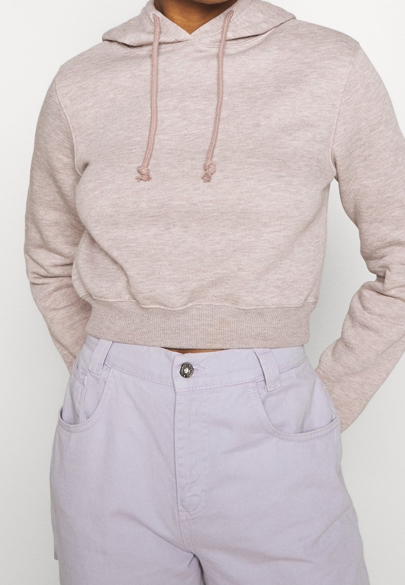 Personne portant un sweat à capuche court beige clair avec cordons et un pantalon taille haute lavande clair avec bouton et poches.