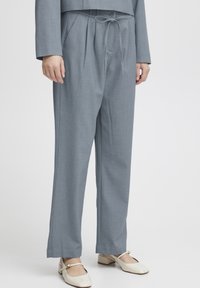 Graue maßgeschneiderte Hose mit lockerem Schnitt, ausgestattet mit einem Kordelzugbund, seitlichen Taschen und glatter Stoffstruktur.
