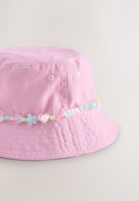 Rosa Baumwoll-Bucket-Hut mit multicolor Pastellperlen in Form von Herzen, Sternen und Blumen, die um die Krone gefädelt sind.
