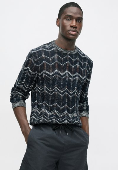 Granatowy sweter na drutach z wzorem jodełki, z kontrastującymi białymi i rdzawego koloru akcentami oraz prążkowanym okrągłym dekoltem.