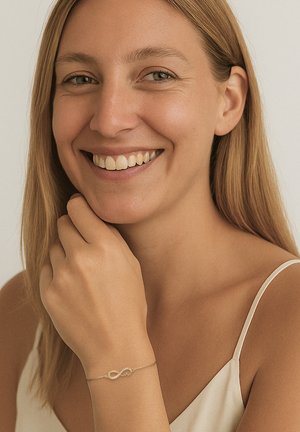 Bracciale in oro con simbolo dell'infinito, caratterizzato da piccoli accenti di perle. Indossato su una mano, con tono di pelle chiaro e texture liscia.