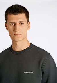 Sudadera gris oscuro con escote redondo y puños de canalé. Presenta "LINDBERGH" bordado en gris claro en el pecho. Textura suave.