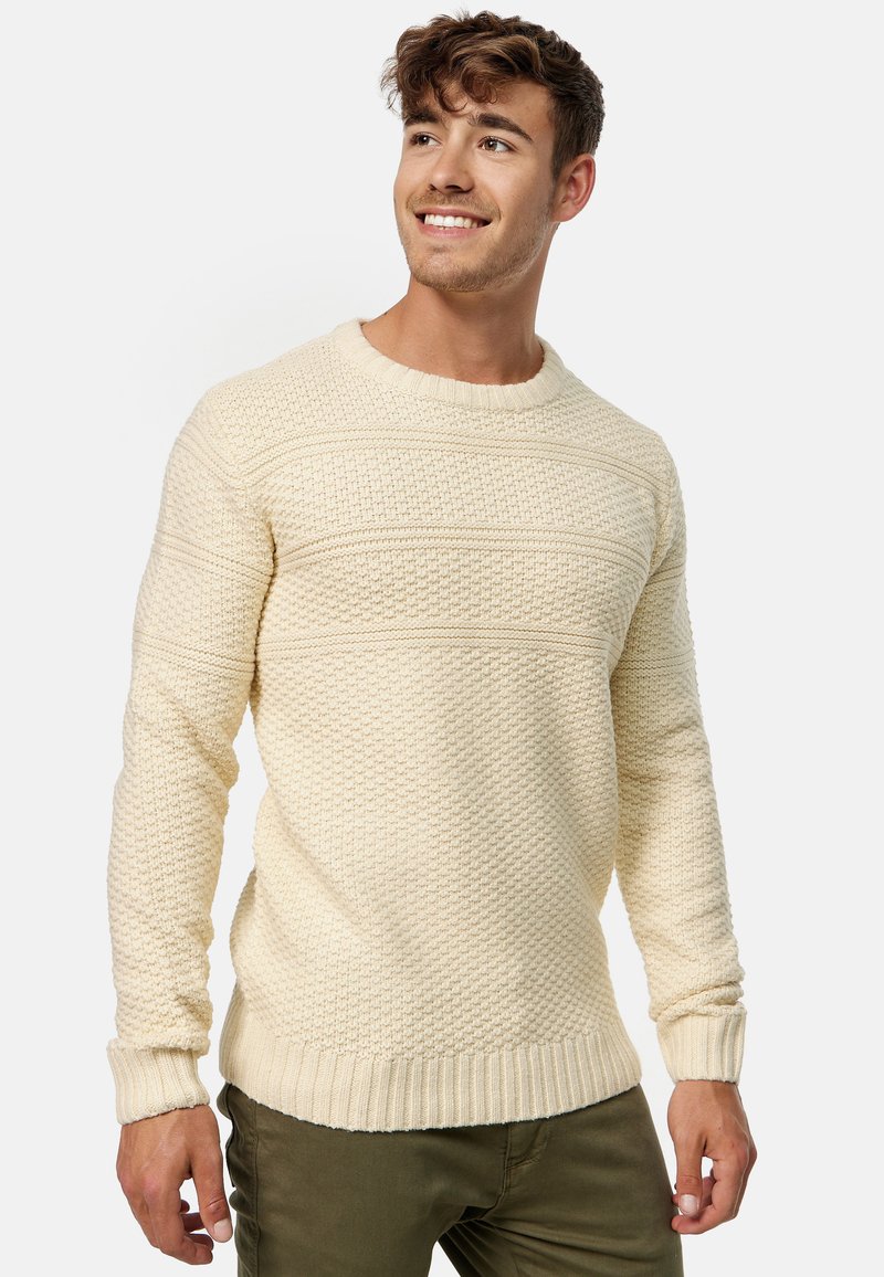 Jersey de punto de color crema con patrón texturizado, cuello redondo y puños y dobladillo acanalados. Diseño ajustado de grosor medio.