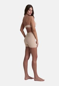 Beige naadloze bandeau top en high-waisted shorts van rekbaar materiaal, met een witte textuur en een minimalistisch ontwerp.