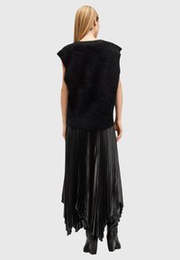 Black sleeveless sweater with a fuzzy texture, paired with a long black pleated skirt that drapes asymmetrically, and knee-high boots.