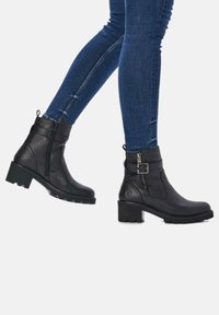 Black leather ankle boots with a textured finish, side zipper, and buckle accent. Chunky, contrasting black rubber sole.