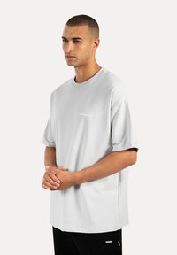 T-shirt oversize grigio chiaro con colletto a girocollo, realizzata in tessuto morbido. Caratterizzata da maniche corte e un piccolo logo sul petto.