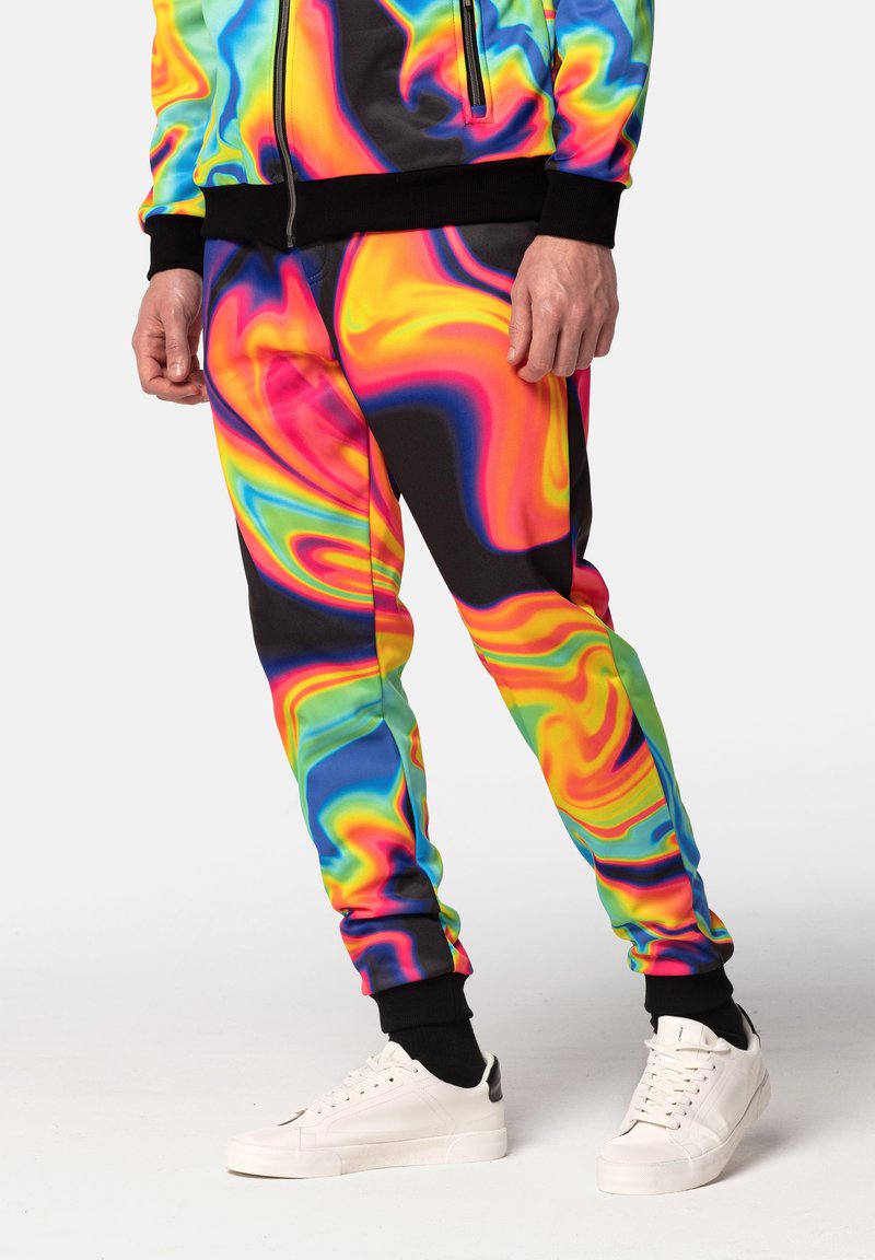 Multifarvet psykedelsk tracksuit med svungne mønstre i pink, sort og grøn; designet med elastiske manchetter og parret med hvide sneakers.
