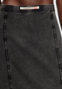 Svart denimkjol med en figurnära design, synlig sömnad och en märkesskärp. Tyget har en slät textur med minimal slitage.