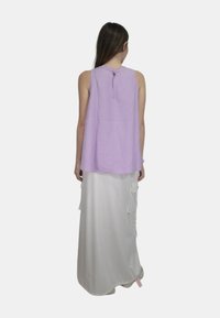 Top senza maniche di lavanda con scollatura alta e dettagli di bottoni sul retro, abbinato a una lunga gonna bianca con tasche laterali e una texture liscia.
