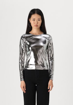 Zilveren lange mouwen top met een glanzende, metalen afwerking; aansluitend ontwerp met een gladde textuur. Gecombineerd met zwarte broeken met versieringen.
