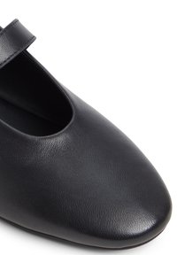 Chaussures en cuir noirs avec un bout arrondi, présentant un design découpé et une sangle unique sur le dessus pour un maintien sécurisé. Texture lisse.